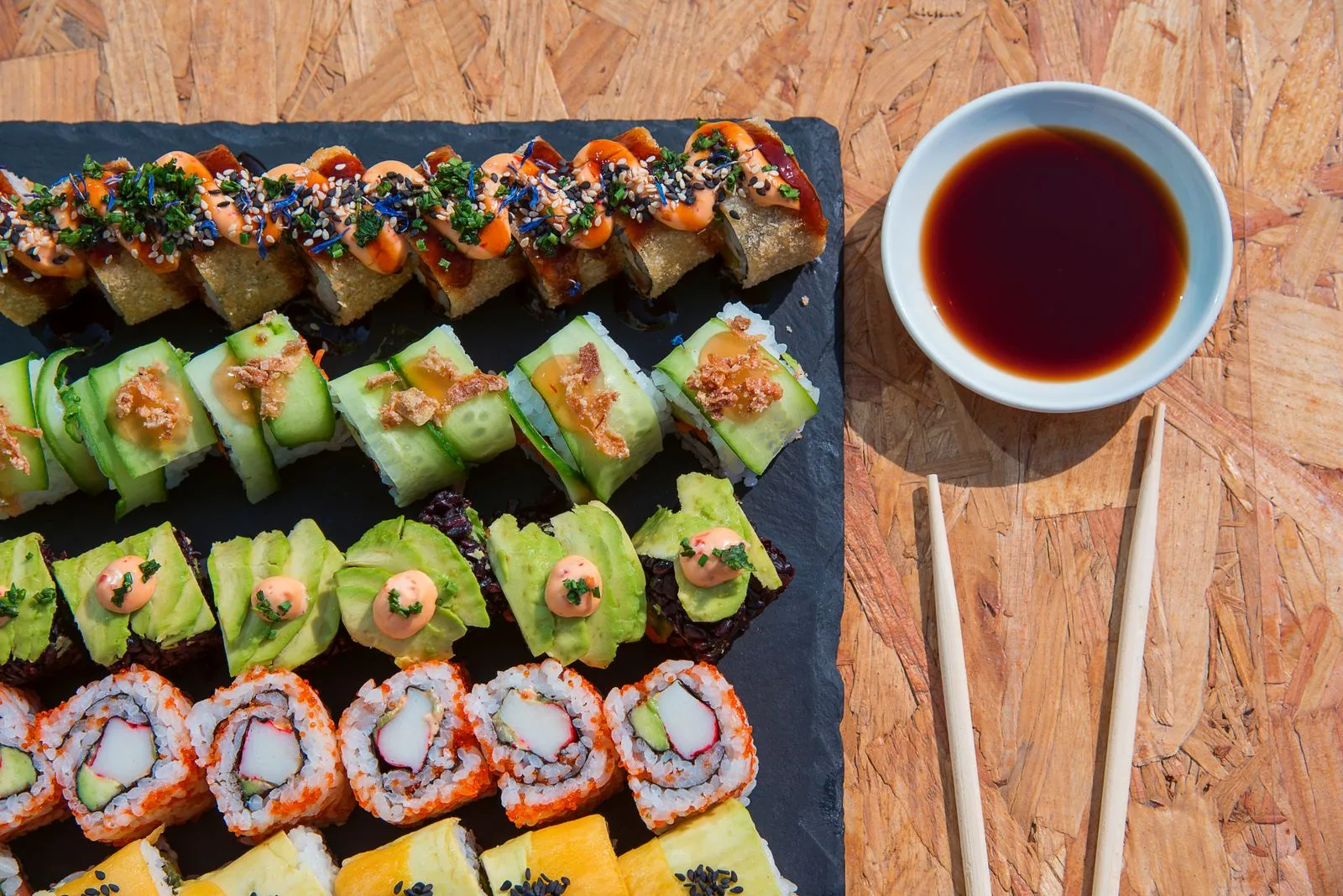 A vibrant assortment of sushi rolls with a bowl of soy sauce.